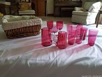 Wide view of cranberry glassware with woven basket and fabric liner on white cloth in living room setting.