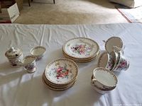 Full view of the lot showing side plates, cups, saucers, and containers arranged on a white cloth.