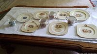 Overview of all items on white cloth, showing plates and mugs with British royal imagery and gold trim