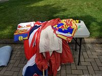 Various folded and draped flags displayed on a white folding table with some flags spilling into a blue plastic bin beneath.