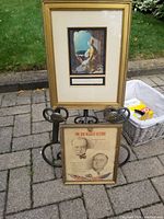 Overview photo showing both framed prints displayed outdoors on a paved surface, one larger gold-framed George Baxter print titled Xenoboa, and a smaller framed vintage print with portraits of Churchill and Roosevelt