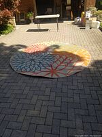 Photo showing the round carpet laid on outdoor brick paving, illustrating the full floral design and scale.