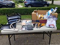 Photo of entire lot on table showing document trays, power strip, calculators, box of office supplies, and tools.