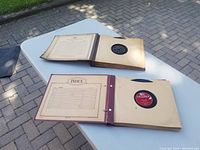 Wide view of two albums holding 78 RPM records, open on a white table outdoors, showing pages with records in sleeves.
