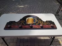 Top view of the wooden pub sign featuring painted gold text and a 3D ale mug with six knobs for coats.