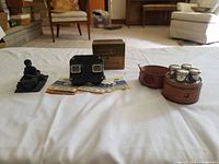 Photo of all items showing the vintage viewfinder with reels, leather case with four perfume bottles, and coal bathing figure in a bathtub.