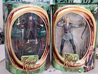 Photo showing both action figures in original packaging side by side: Frodo Baggins on left, Legolas on right.