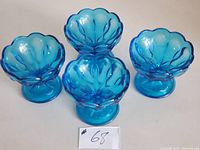 Four vintage blue glass comports arranged on a white surface, visible scalloped edge and pedestal bases.
