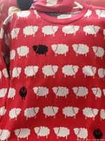 Close-up front view of red sweater with repeated pattern of white sheep and a few black sheep