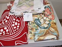 Folded fabric pieces showcasing a red fabric with white dots, floral patterns in peach and teal, and abstract pastel design.