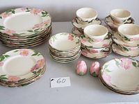 Photo showing stacks of various Franciscan Desert Rose plates, cups, saucers, and rose bud shaped salt and pepper shakers arranged on table.