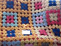 Full view of quilt showing color coded square pattern composed of hand stitched circular fabric yo-yos in blue, pink, and beige.