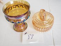 Photo of amber glass swan covered trinket/powder box next to iridescent carnival glass footed candy dish on white background.