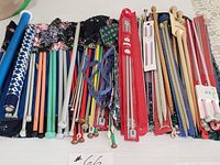 Wide view showing various knitting needles in different materials and colors, along with several fabric needle holders.