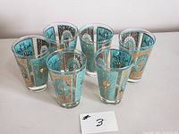 Photo of six turquoise and gold decorated drinking glasses arranged in two rows showing design and condition.
