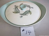 Top angle photo of the casserole dish showing the leaf and flower decoration on the lid and part of the turquoise rim dish.