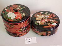 Two red and black lacquer containers with floral and fan designs, one three-tiered and one single-lid.