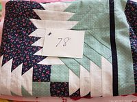 Folded geometric patterned quilt top with green, cream, and dark blue floral fabric showing the style and condition.