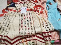 Close-up of hand-crocheted cream and red half apron with red ribbon ties over other patterned fabric aprons