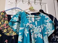 Three vintage floral house dresses hanging on a rack, showing different floral patterns and colors.