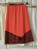 Lot of six vintage half slips hanging on hangers; coral half slip has black lace hem and bow detail, others in white and cream colors