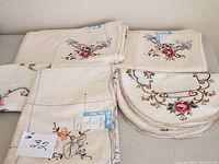 Full view showing multiple folded hand embroidered linens including tablecloths and placemats stacked together