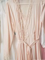 Light pink vintage robe hanging on hanger, showing scalloped neckline and tie belt
