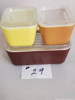 Three vintage refrigerator dishes stacked, showing yellow, orange, and brown colored dishes with ribbed plastic lids.