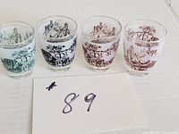 Four frosted shot glasses with distinct printed scenic images and colors on a white surface.