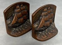 Pair of cast iron bookends featuring raised ship design and bronze coloring, showing front and side views.