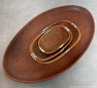 Top-down photo showing the three oval nested wooden bowls with white inlaid designs inside the large oval wooden tray.