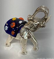 Elephant figurine front right side view showing silver body and vibrant glass saddle with colorful floral designs.