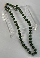 Dark green jade beads strung and draped over clear acrylic stand.
