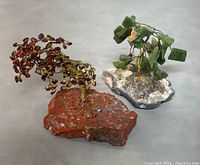 Photo showing both decorative gemstone trees, one with green jade leaves on amethyst base and the other with red jasper leaves on red jasper base, highlighting their size and color contrast.