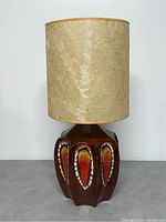 Full view of retro pottery glaze table lamp showing brown multi-faceted base with orange and white teardrop pattern, topped with beige textured lampshade.