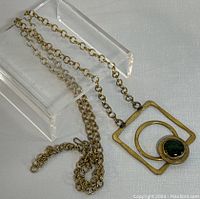 Full view of the 28-inch brass link chain and geometric pendant with a green stone.