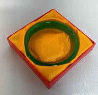Green jade bangle in red box with yellow satin interior showing condition and presentation.