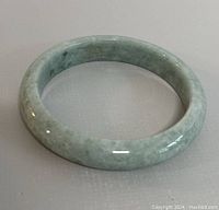 Natural jade bangle bracelet shown from an angle on a plain background, highlighting its shape and coloration.