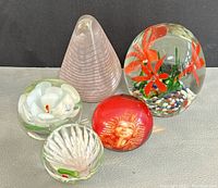 Collection of five paperweights on a fabric surface including floral, pharaoh image, and pyramid shaped pieces.