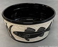 Side view of ceramic art pottery bowl showing black fish and plant motif against textured white background.
