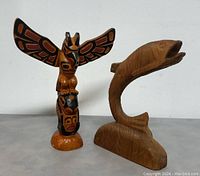 Two carved wooden sculptures side by side, fish on right and painted totem pole on left