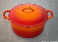 Front angle view of the orange-red enameled cast iron pot with lid and dual side handles.