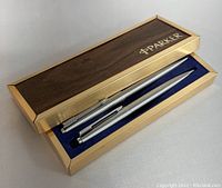 Open pen case showing two silver-tone pens inside, blue velvet lining