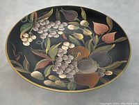 Oval porcelain platter with black background and colorful hand painted fruits and leaves, viewed from above