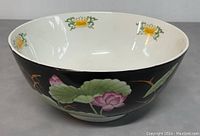 Front side view of porcelain salad bowl showing hand painted lotus flowers and green leaves on black background