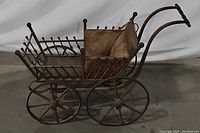 Side view of the antique baby doll buggy showing the wooden and metal construction with four spoked wheels and spindle detailing.