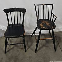 Pair of black antique wooden chairs: a hand stenciled side chair and a Windsor armchair, both showing clear paint wear.
