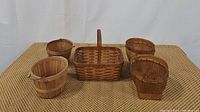 Five berry picking baskets laid out on a woven mat background including round peck baskets, small woven handled baskets, and a pie basket.