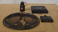 Four black antique items displayed together on textured surface: thermos, document box, hinged box, and painted oval platter.