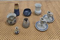 Seven ceramic items displayed on a woven textured surface including pitchers, vases, candle holders, and a dish in blue and neutral tones